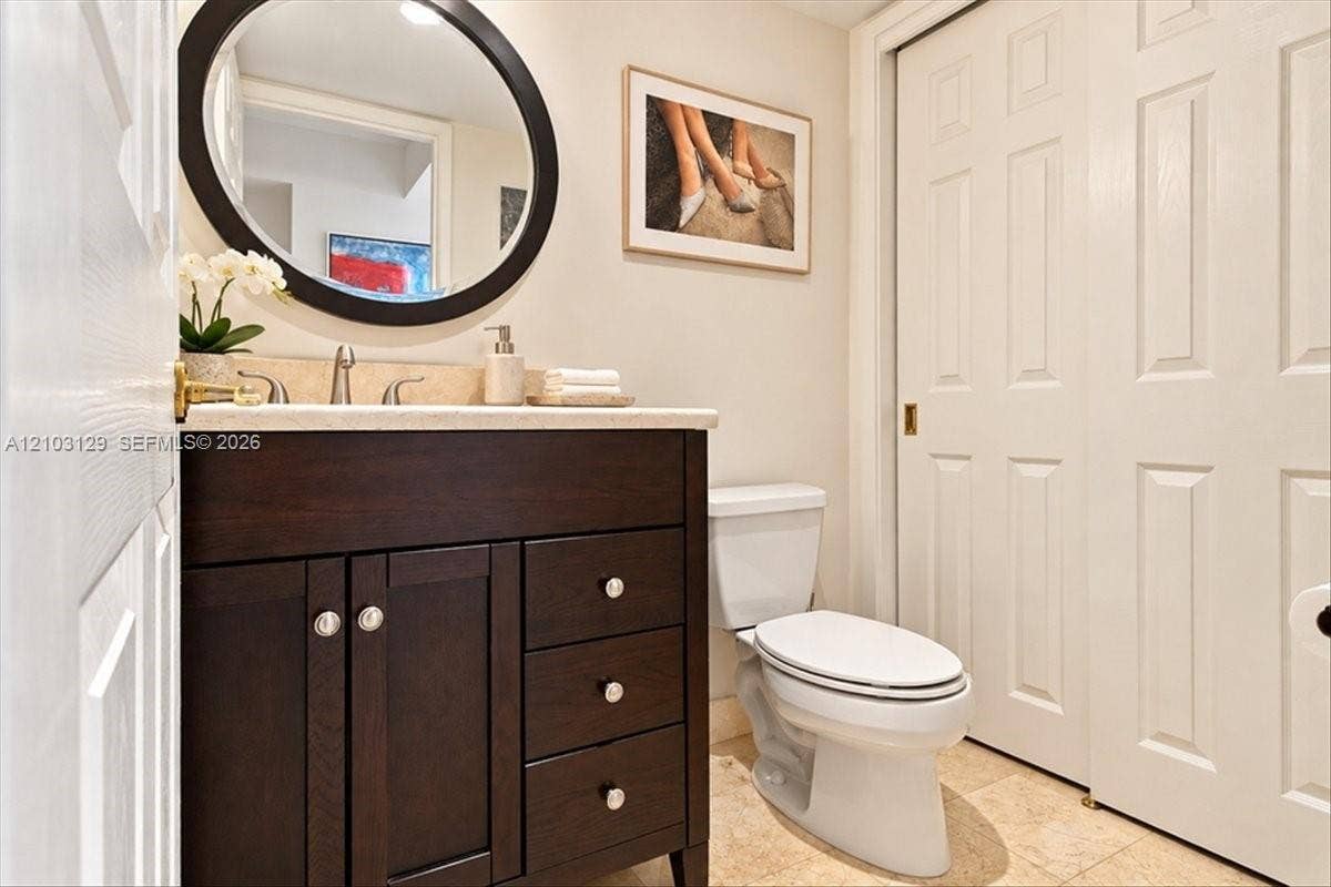 1627 Brickell Avenue, #2005, Miami, FL 33129 Dark wood vanity with a stone countertop, oval wall-mounted mirror, neutral stone flooring, and white two-panel closet doors