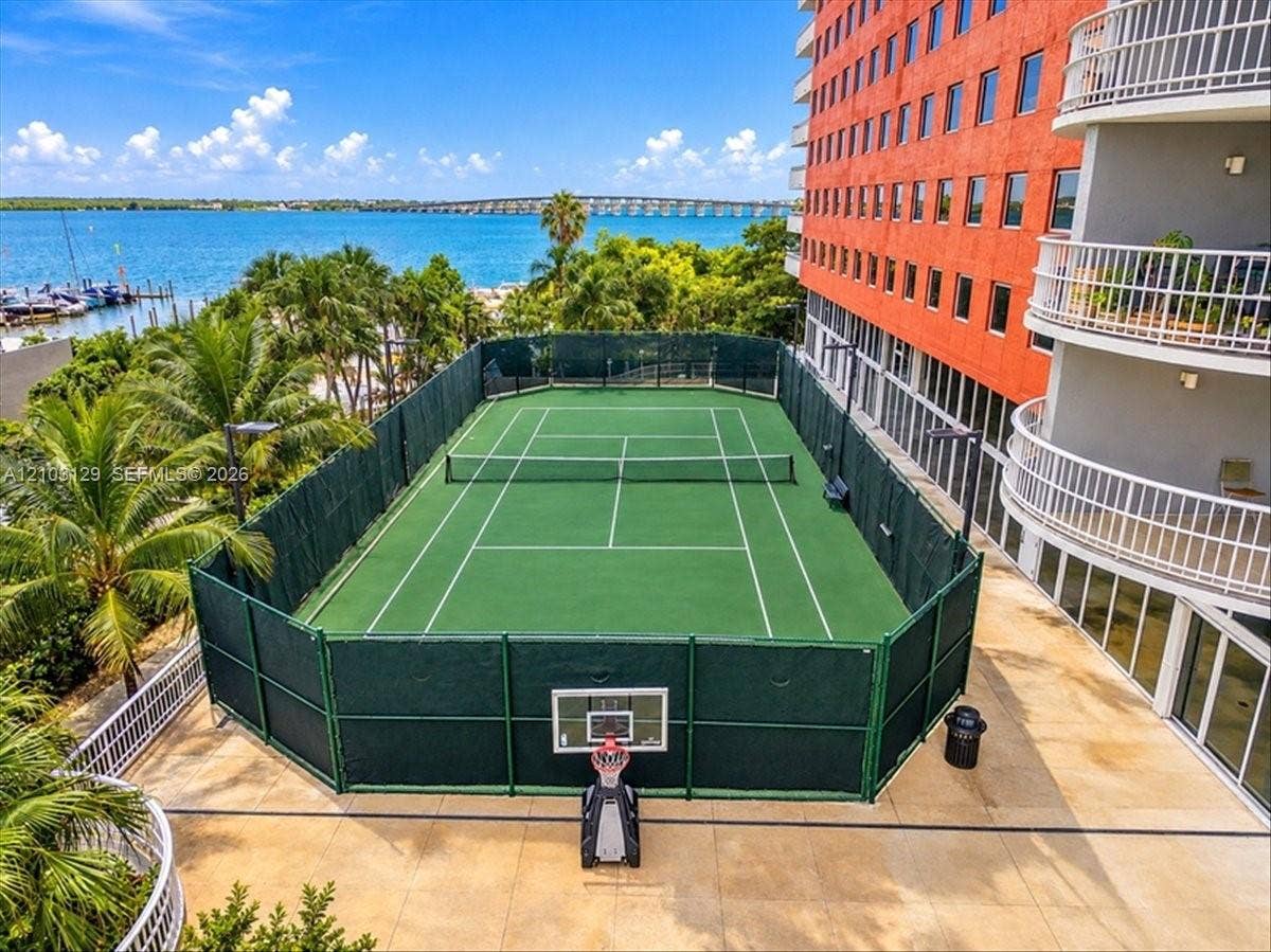 1627 Brickell Avenue, #2005, Miami, FL 33129 Tennis court enclosed by perimeter fencing, featuring a basketball hoop, set against a waterfront backdrop with established palm trees