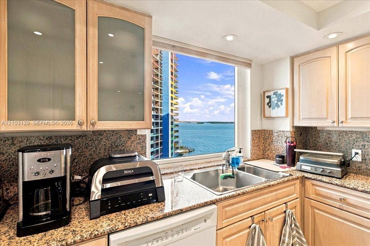 1627 Brickell Avenue, #2005, Miami, FL 33129 Kitchen featuring light wood cabinetry with frosted glass inserts, speckled stone countertops, dual-basin stainless steel sink, and recessed lighting