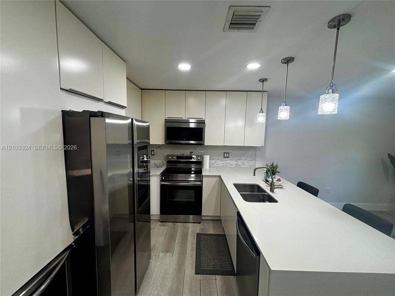 13413 SW 256th Street, Homestead, FL 33032 Kitchen featuring flat-panel cabinetry, quartz countertops, a double-basin stainless steel sink with a pull-down faucet, stainless steel appliances, and wood-finish flooring