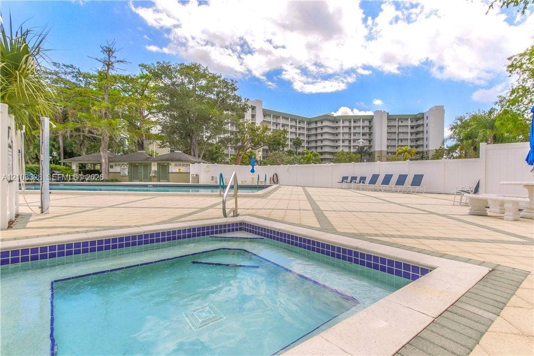 In-ground spa with blue tile surround, paved pool deck, swimming pool, and dedicated covered cabana area