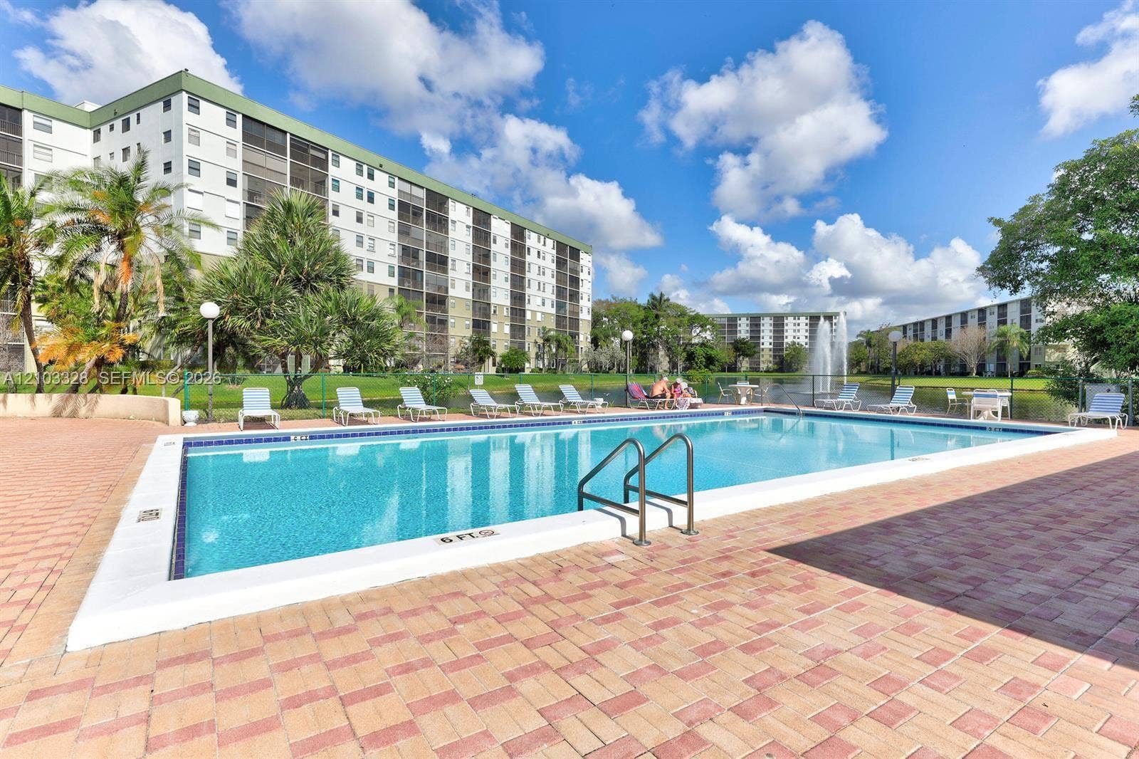 Swimming pool featuring a paved deck, metal railings, and a water feature backdrop