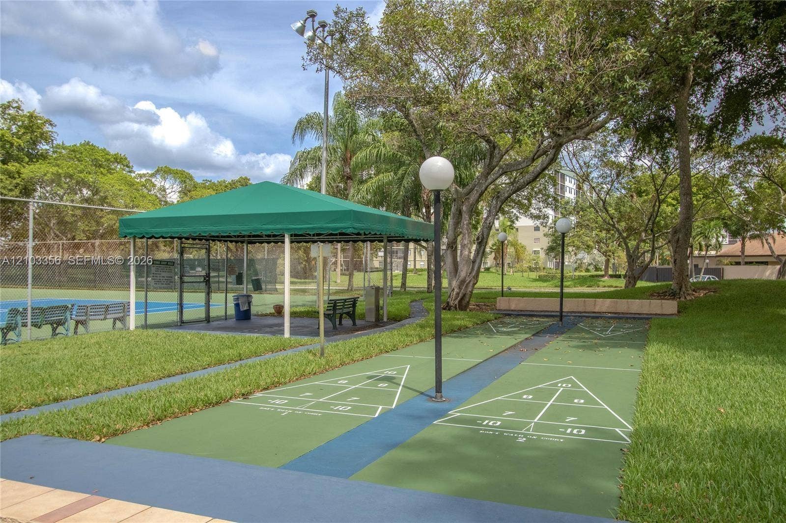 Recreational area featuring dual shuffleboard courts, a covered pavilion, and a fenced hard-surface court