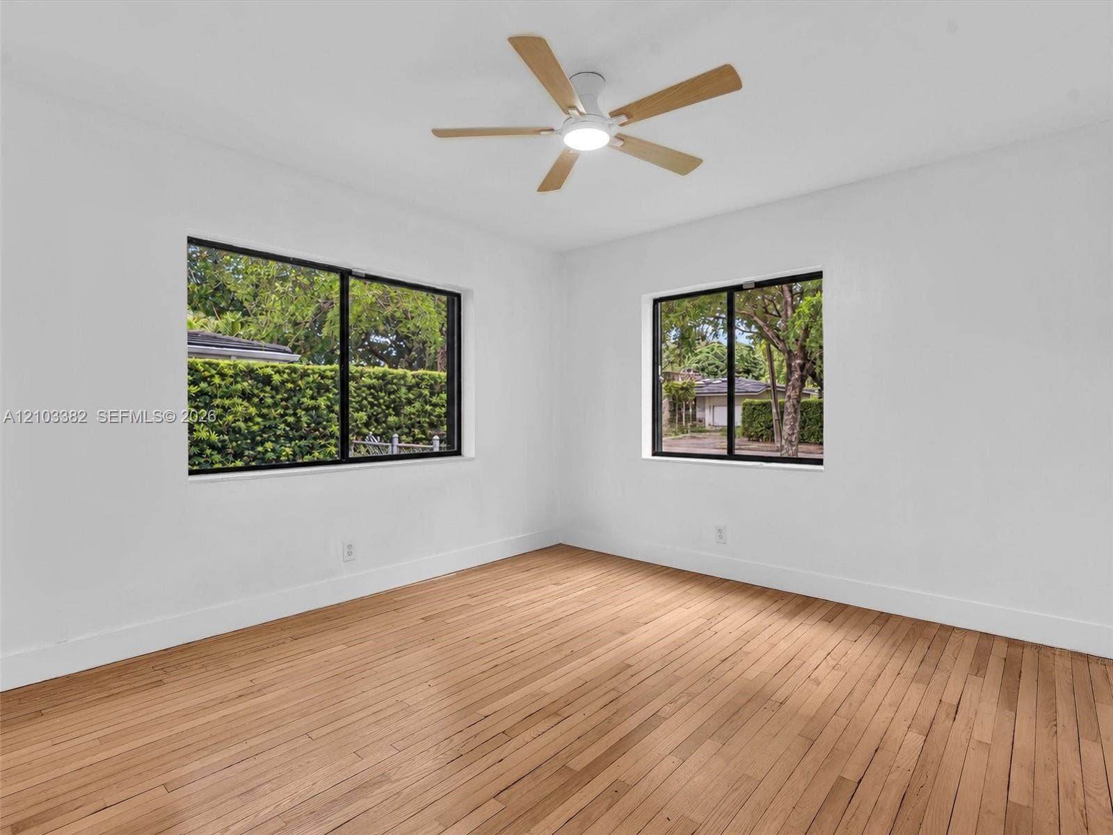 1545 Mantua Avenue, Coral Gables, Coral Gables, FL 33146 Large front/east bedroom with sunny windows. Featuring wood-finish flooring, two windows with black frames, and a multi-blade ceiling fan with integrated lighting. House for rent in Coral Gables. House for rent listed by Realtor.
