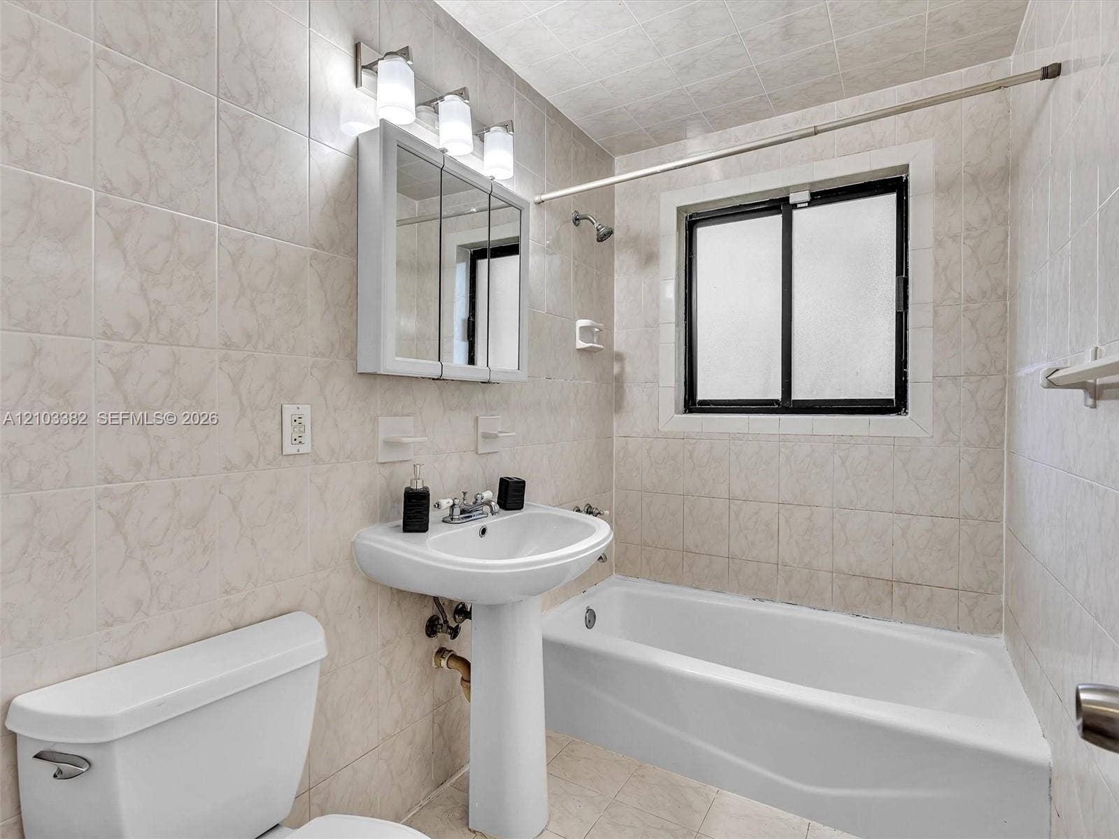 1545 Mantua Avenue, Coral Gables, Coral Gables, FL 33146 Full bathroom featuring a pedestal sink, a bathtub with a tiled surround, a mirrored medicine cabinet with integrated lighting, and a window