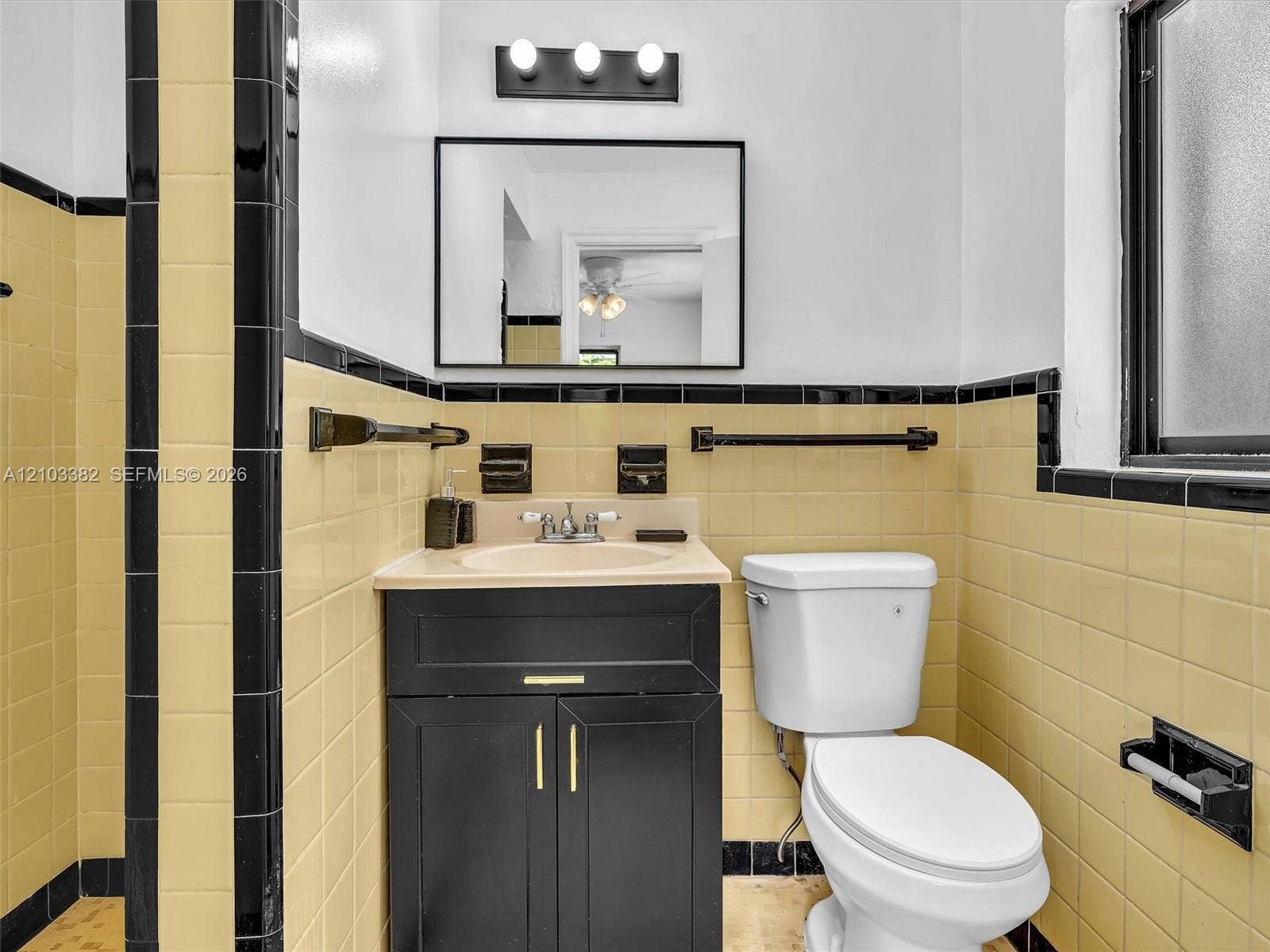 1545 Mantua Avenue, Coral Gables, Coral Gables, FL 33146 Black vanity cabinet with brass-tone hardware, rectangular wall-mounted mirror, three-light fixture, and ceramic tile wall accents featuring contrasting border detailing. House for rent in Coral Gables. House for rent listed by Realtor.