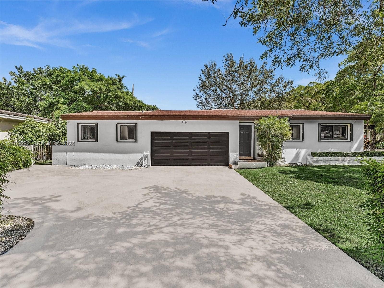 1545 Mantua Avenue, Coral Gables, Coral Gables, FL 33146 Single-story exterior featuring white stucco siding, a flat roofline, attached multi-car garage, concrete driveway, and manicured lawn. House for rent in Coral Gables. House for rent listed by Realtor
