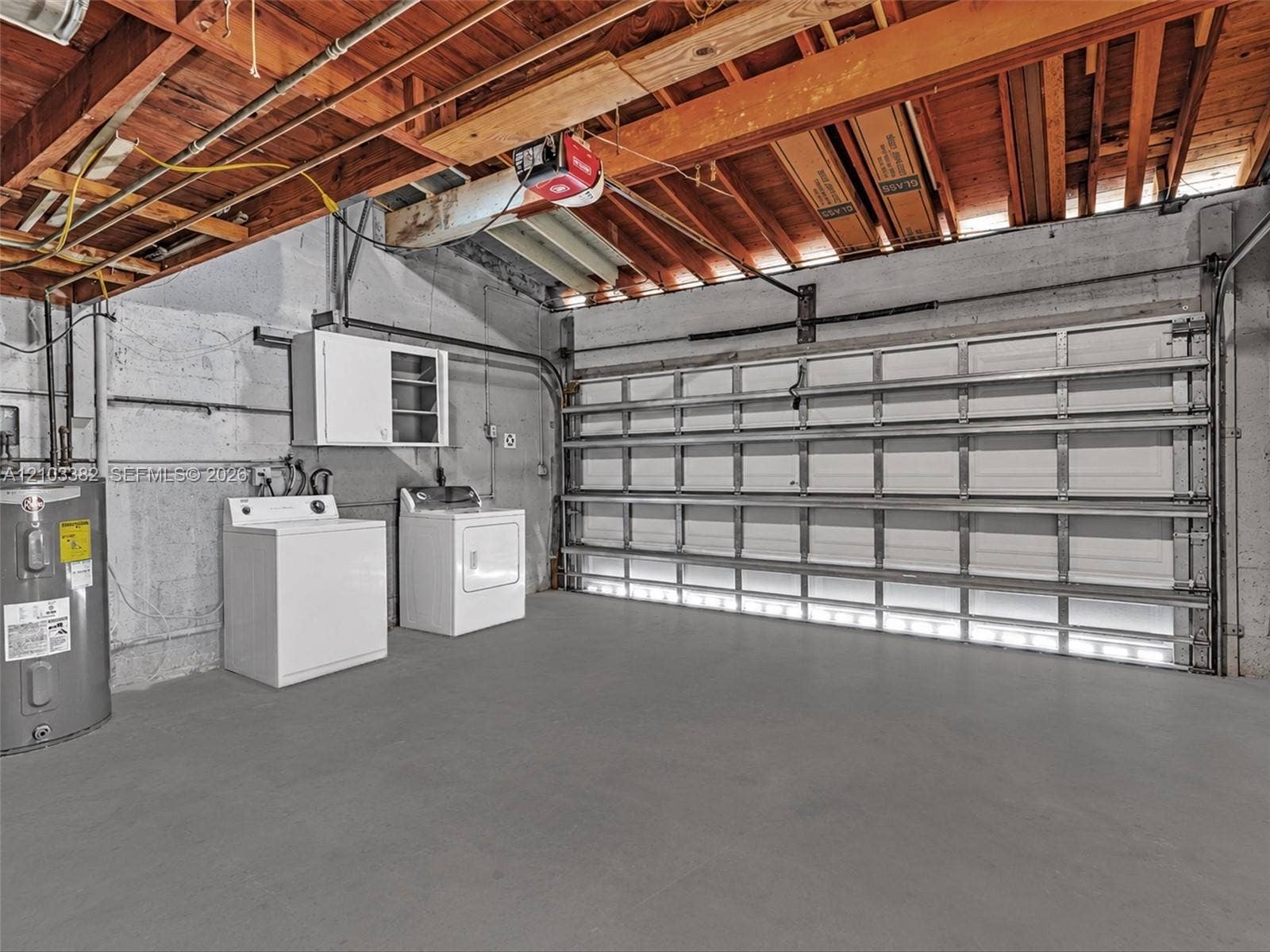 1545 Mantua Avenue, Coral Gables, Coral Gables, FL 33146 Huge 2 car, attached garage featuring a white sectional roll-up door, exposed wood joist ceiling, concrete walls, and concrete flooring. House for rent in Coral Gables. House for rent listed by Realtor.
