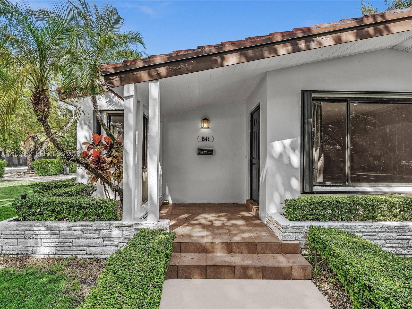 1545 Mantua Avenue, Coral Gables, Coral Gables, FL 33146 Exterior featuring a covered entryway with ceramic tile steps, white stucco siding, stacked stone landscaping walls, and a large picture window. House for rent in Coral Gables. House for rent listed by Realtor