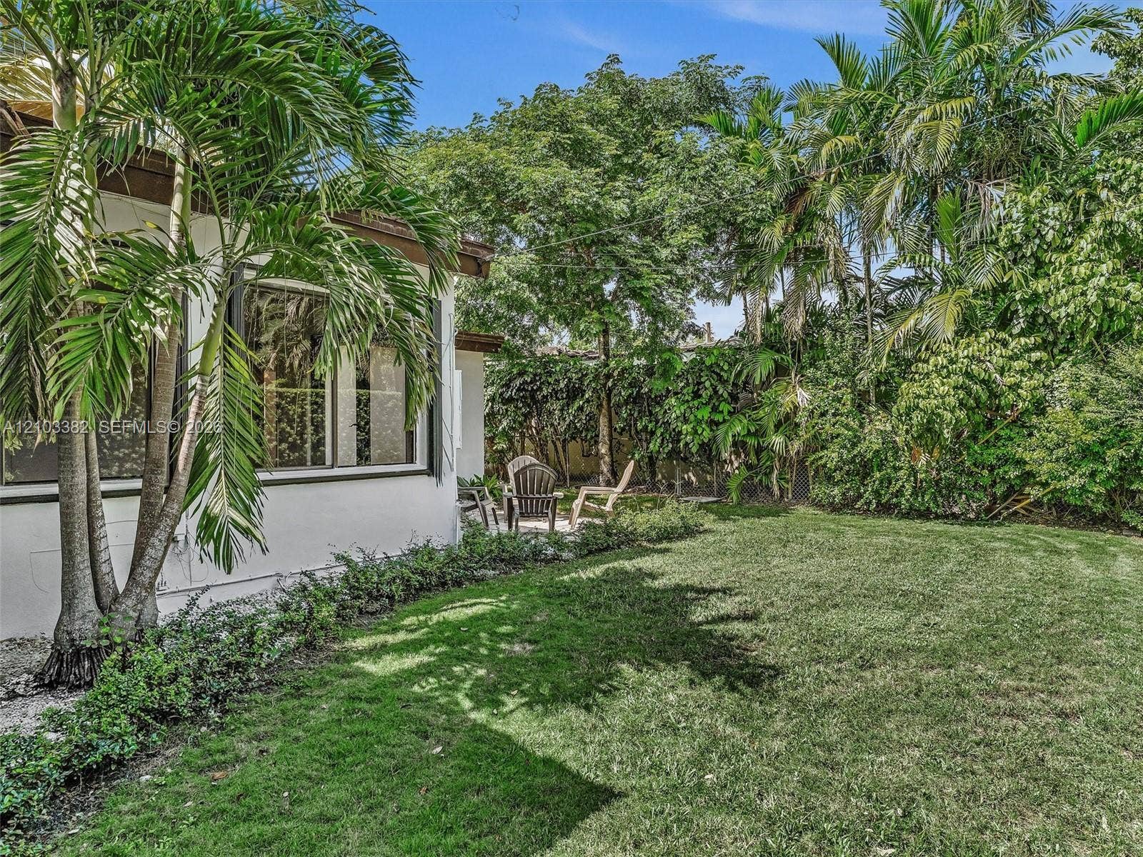 1545 Mantua Avenue, Coral Gables, Coral Gables, FL 33146 Expansive fenced backyard featuring a manicured lawn, established palm trees, mature greenery, and a concrete patio area. House for rent in Coral Gables. House for rent listed by Realtor.