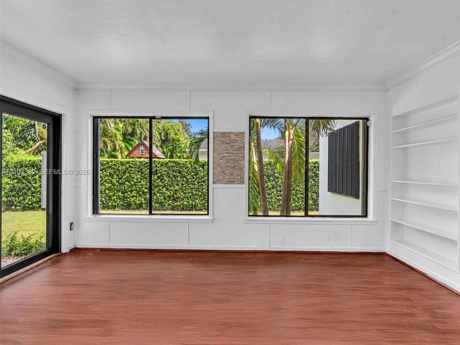 1545 Mantua Avenue, Coral Gables, Coral Gables, FL 33146 Florida room featuring wood-finish flooring, white panel-style wall detailing, large sliding glass doors, dual windows with black frames, and custom built-in shelving, and a large picture window. House for rent in Coral Gables. House for rent listed by Realtor.