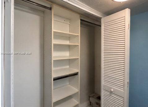Built-in closet featuring white shelving, multiple storage tiers, metal hanging rods, and white louvered doors