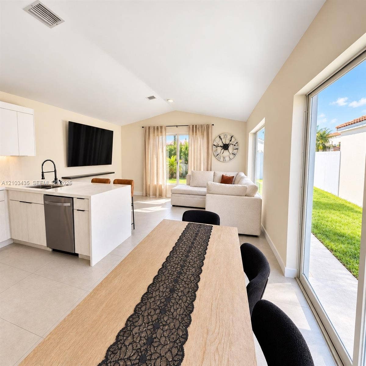 Miami, FL 33177 Open-concept interior featuring light-toned cabinetry, a stone-surface kitchen island with a matte black faucet, vaulted ceilings, and large sliding glass doors providing access to the exterior