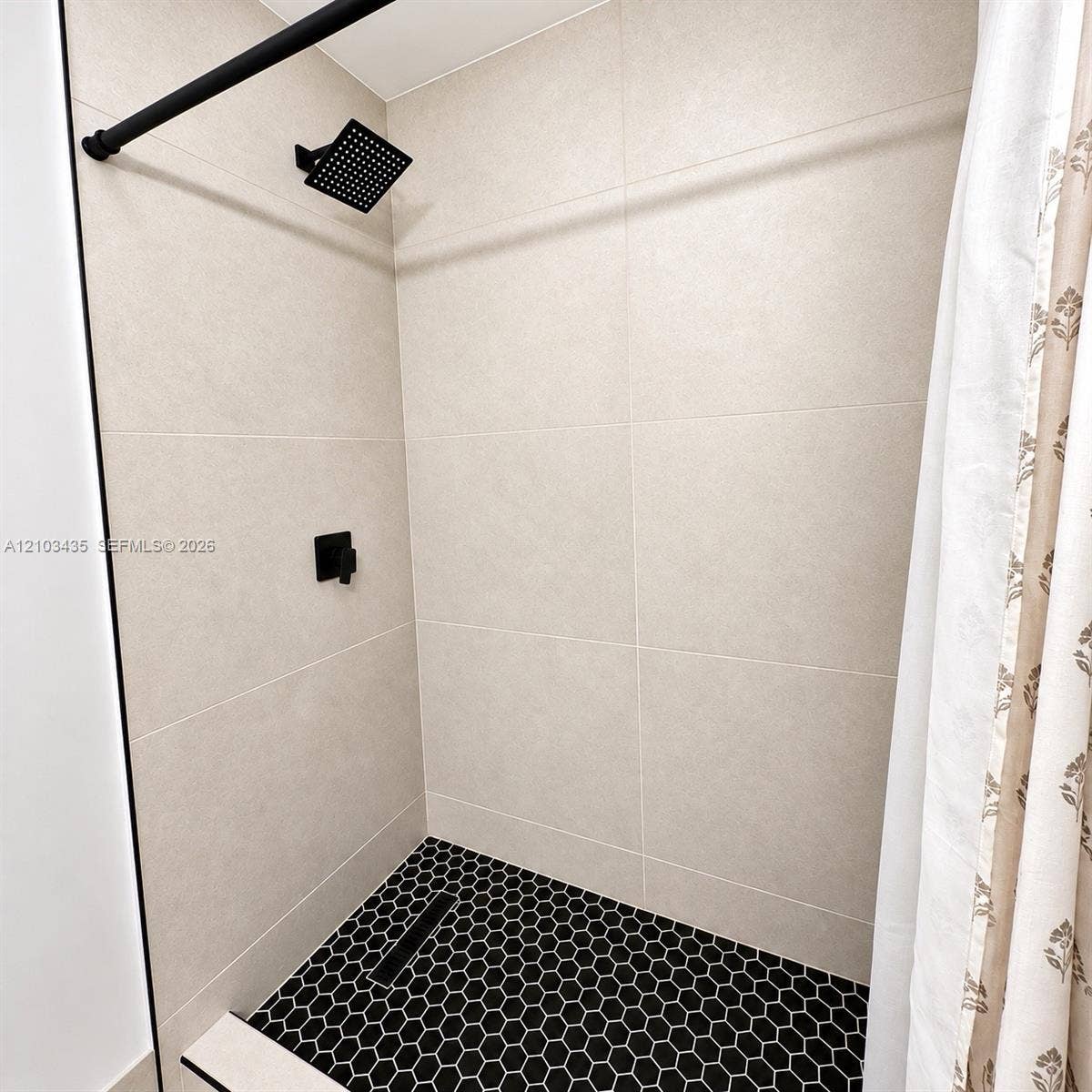 Miami, FL 33177 Shower featuring large-format neutral wall tile, black hexagon floor tile, matte black rain-style shower head, and matte black single-handle mixing valve