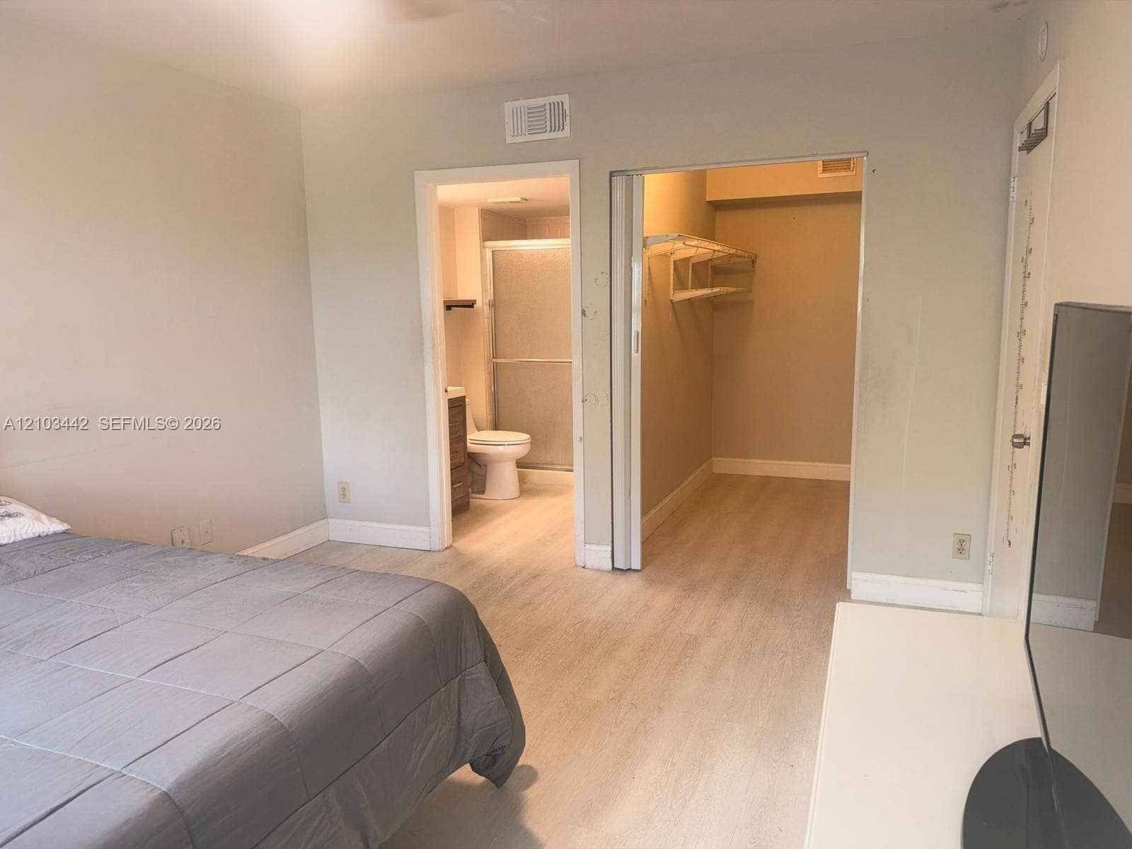 8721 Wiles Road, #303, Coral Springs, FL 33067 Room featuring wood-finish flooring, a walk-in closet with built-in shelving, and a bathroom equipped with a shower enclosure