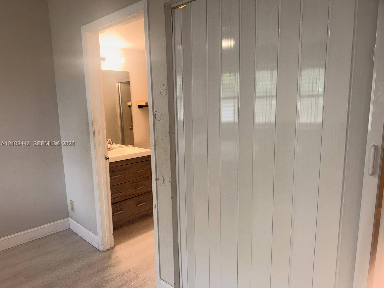8721 Wiles Road, #303, Coral Springs, FL 33067 Vertical-panel sliding door featuring a white finish and wood-finish flooring, incorporating a vanity with a rectangular sink, stone-surface countertop, and lower cabinetry drawers
