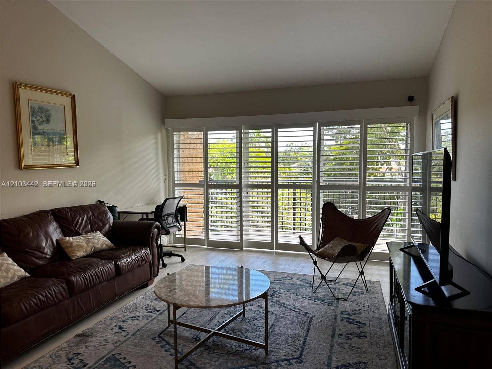 8721 Wiles Road, #303, Coral Springs, FL 33067 Vaulted ceilings and multi-panel floor-to-ceiling sliding glass doors featuring white plantation-style shutters and wood-finish flooring