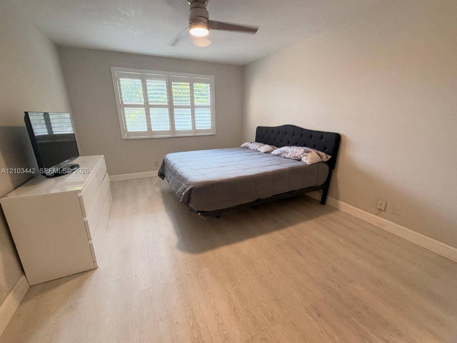 8721 Wiles Road, #303, Coral Springs, FL 33067 Neutral-toned room featuring light-toned wood-finish flooring, plantation shutters, and a central ceiling fan with an integrated light fixture