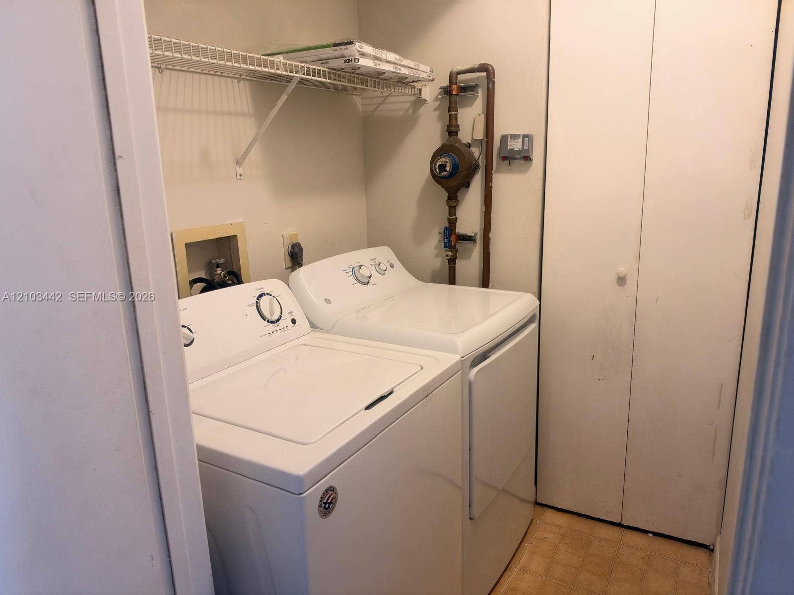 8721 Wiles Road, #303, Coral Springs, FL 33067 Dedicated laundry area featuring a wall-mounted wire storage shelf, bi-fold closet door, and dedicated plumbing hookups