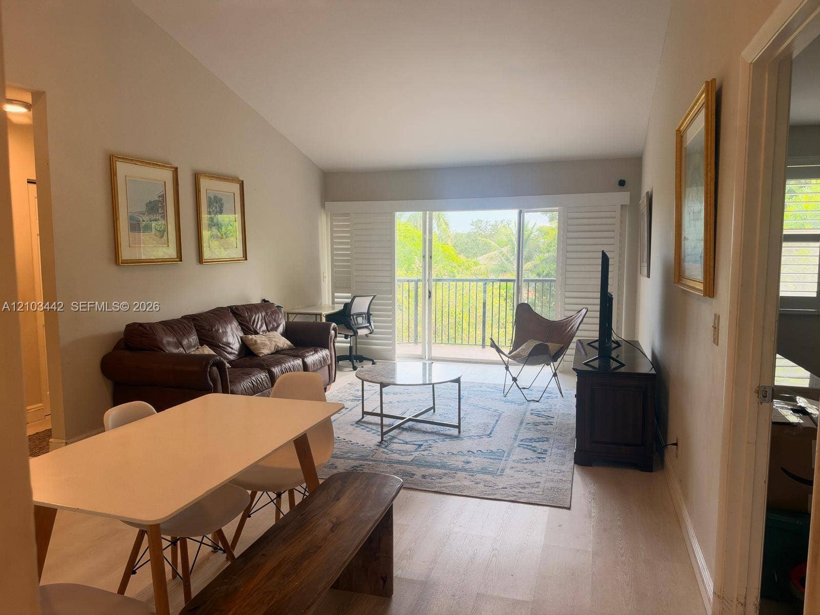 8721 Wiles Road, #303, Coral Springs, FL 33067 Living area featuring vaulted ceilings, light-tone wood-finish flooring, and glass sliding doors with plantation shutters opening to a balcony with iron railings