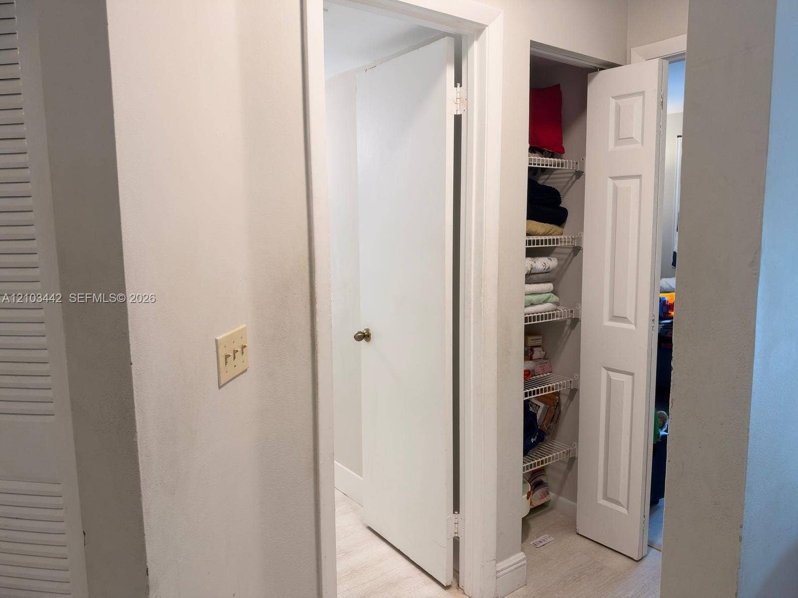 8721 Wiles Road, #303, Coral Springs, FL 33067 Interior hall featuring white six-panel swing doors, a built-in reach-in closet with integrated wire shelving, and wood-finish flooring
