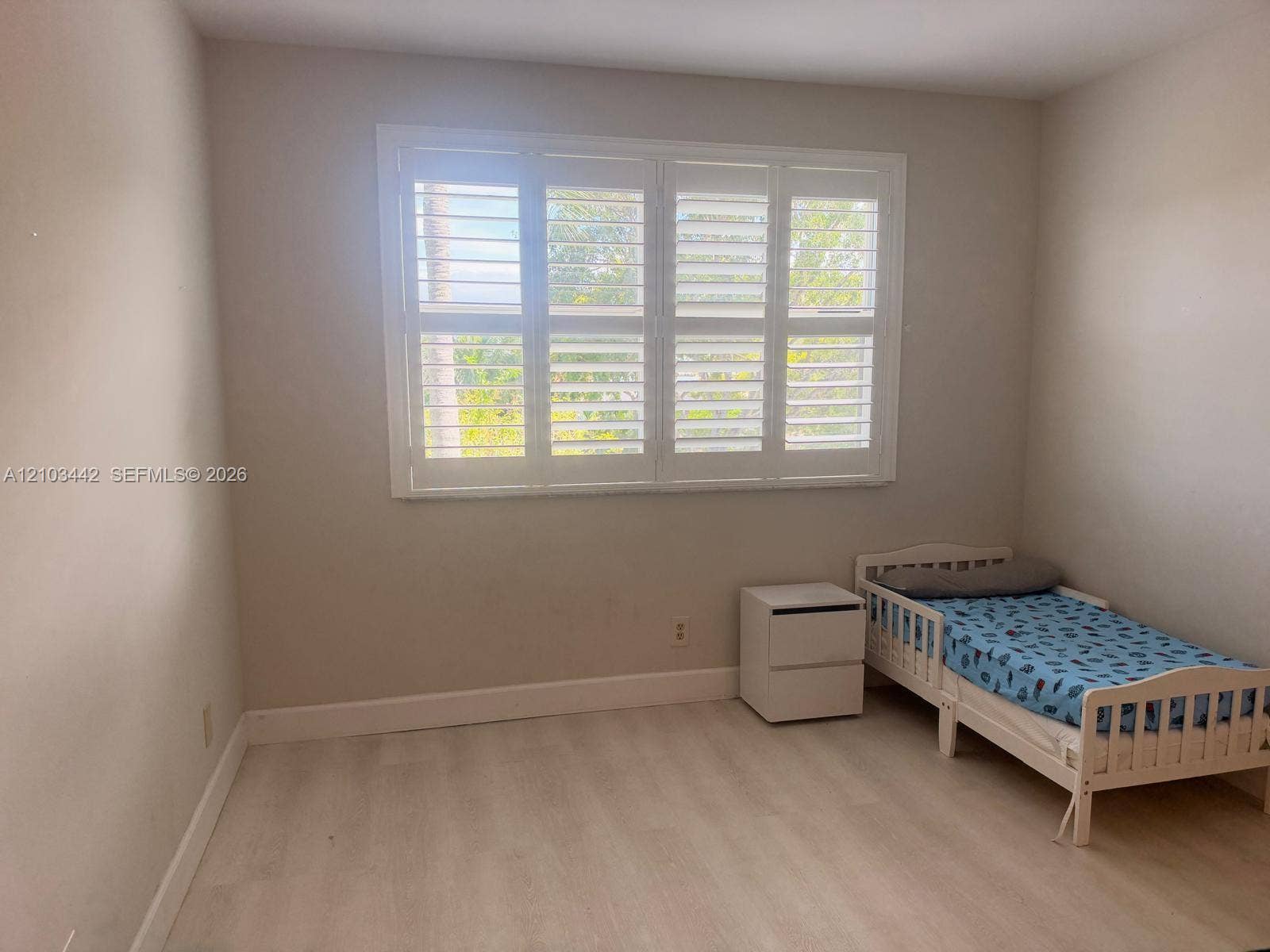 8721 Wiles Road, #303, Coral Springs, FL 33067 Neutral-toned interior room featuring wood-finish flooring and a multi-panel window fitted with white plantation shutters