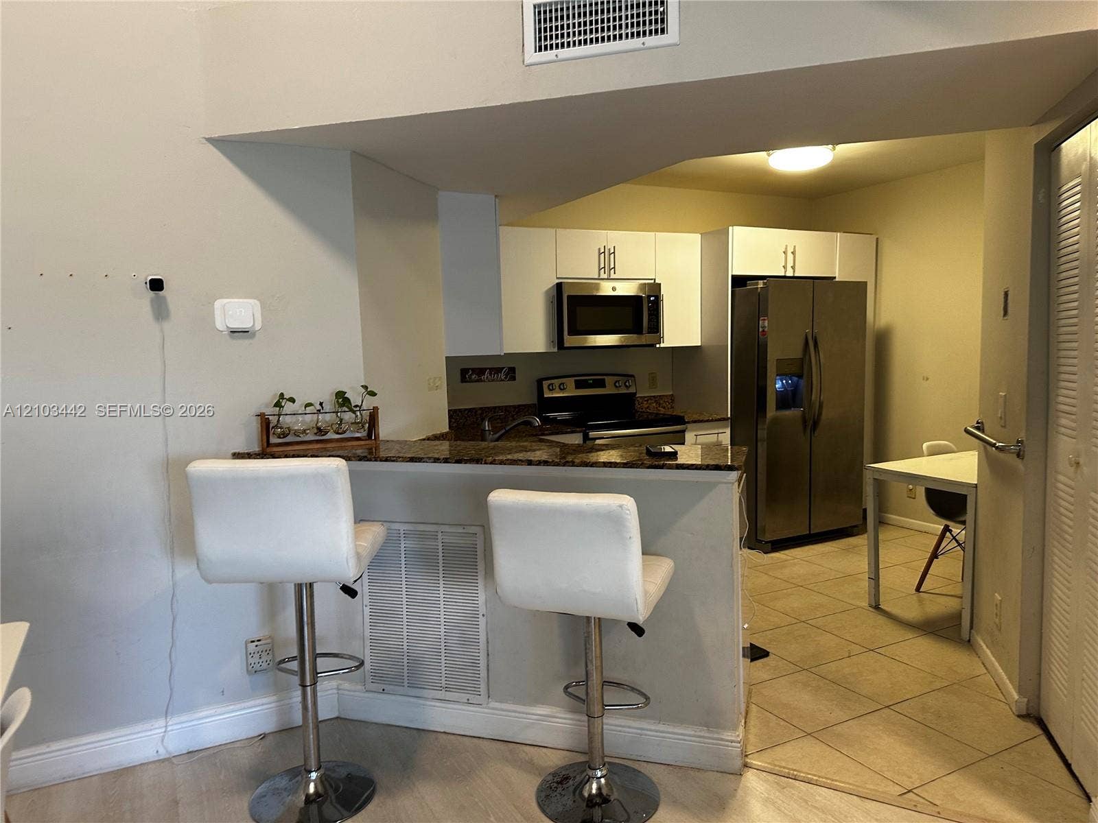8721 Wiles Road, #303, Coral Springs, FL 33067 Kitchen featuring white cabinetry, stone-finish countertops, stainless steel side-by-side refrigerator, built-in microwave, and tile flooring