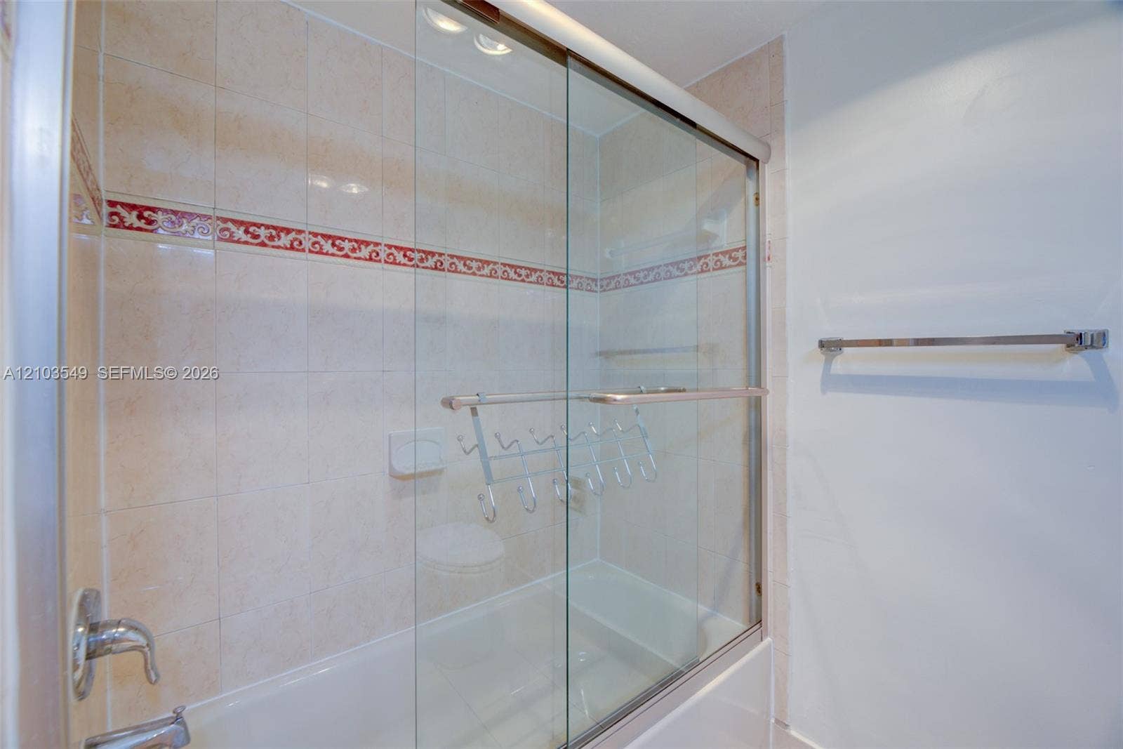 8901 N New River Canal Road, #4W, Plantation, Plantation, FL 33324 Shower-tub combination featuring sliding glass doors, neutral ceramic wall tile, a decorative red accent tile border, and metallic hardware