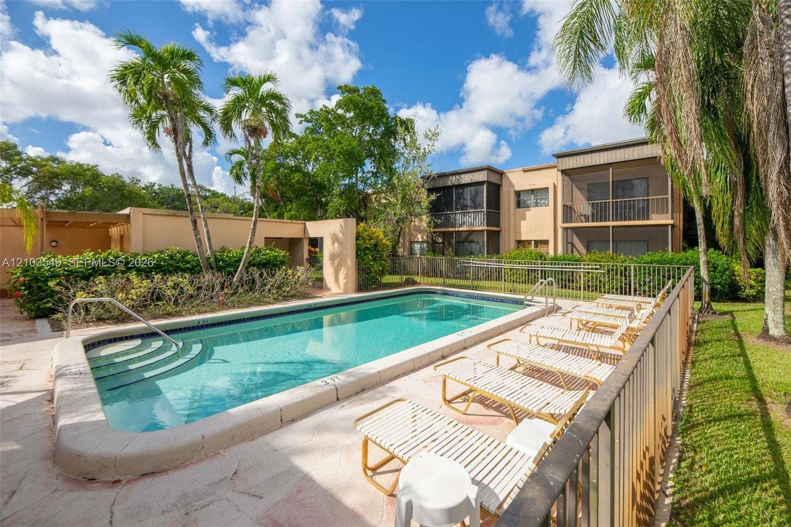 8901 N New River Canal Road, #4W, Plantation, Plantation, FL 33324 In-ground swimming pool with integrated stairs, surrounded by a stone-paver patio, perimeter fencing, and mature palm trees