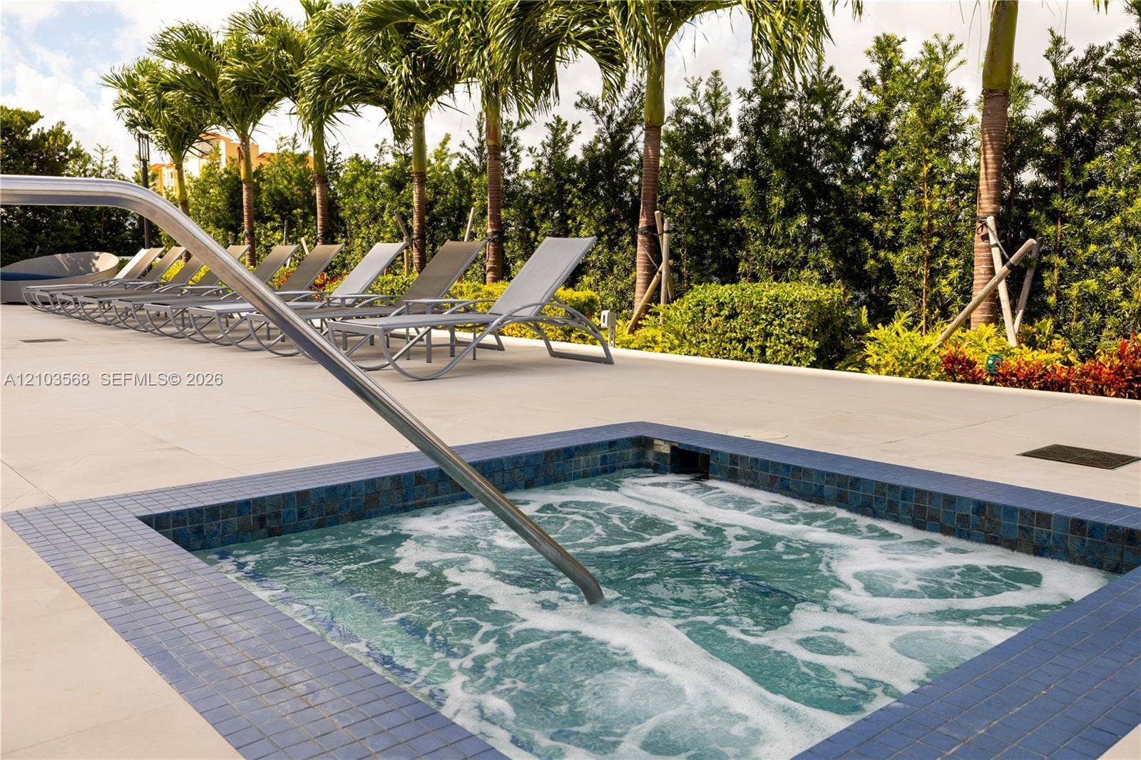 7901 Hispanola Avenue, #801, North Bay Village, FL 33141 In-ground spa with blue tile surround, metal handrail, expansive concrete deck, and mature palm tree landscaping