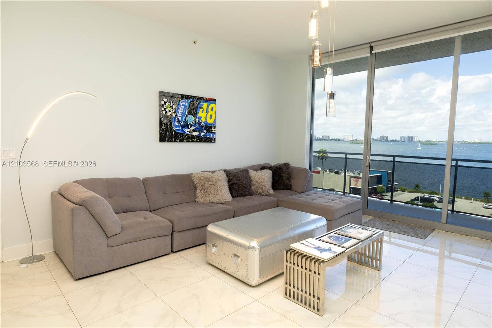 7901 Hispanola Avenue, #801, North Bay Village, FL 33141 Floor-to-ceiling glass sliding doors, polished tile flooring, balcony with metal railing, and multi-pendant contemporary light fixture