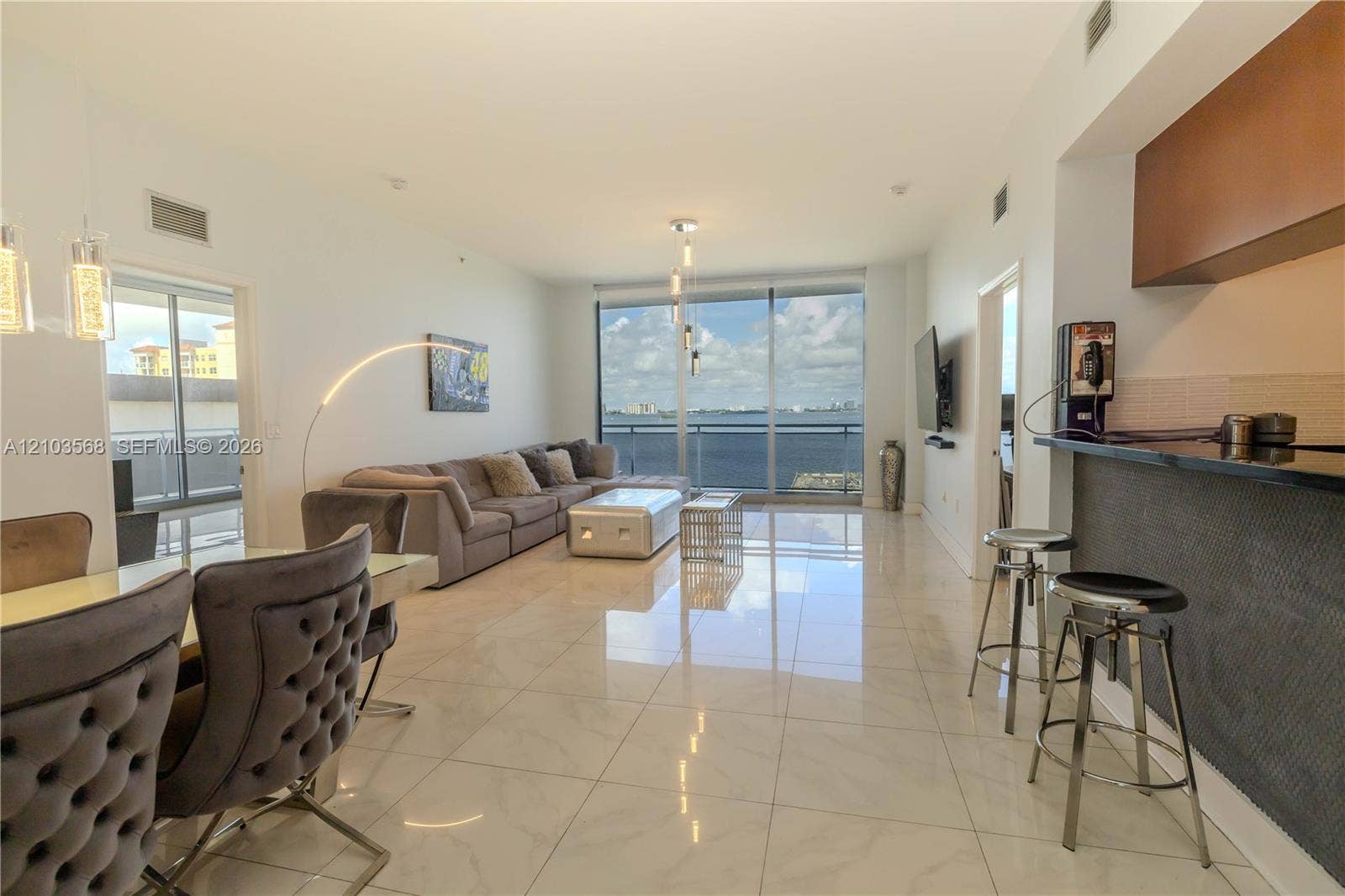 7901 Hispanola Avenue, #801, North Bay Village, FL 33141 Open-concept living area featuring polished tile flooring, floor-to-ceiling windows, a stone-surfaced breakfast bar with dark finish cabinetry, and an attached balcony