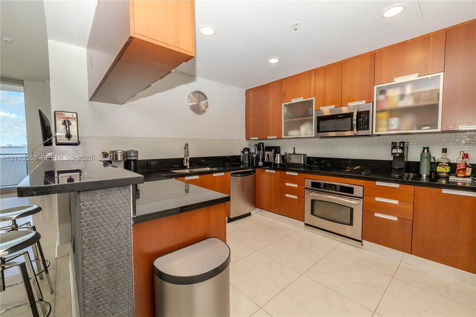 7901 Hispanola Avenue, #801, North Bay Village, FL 33141 Kitchen featuring wood cabinetry, black countertops, stainless steel appliances, tiled flooring, and a peninsula breakfast bar