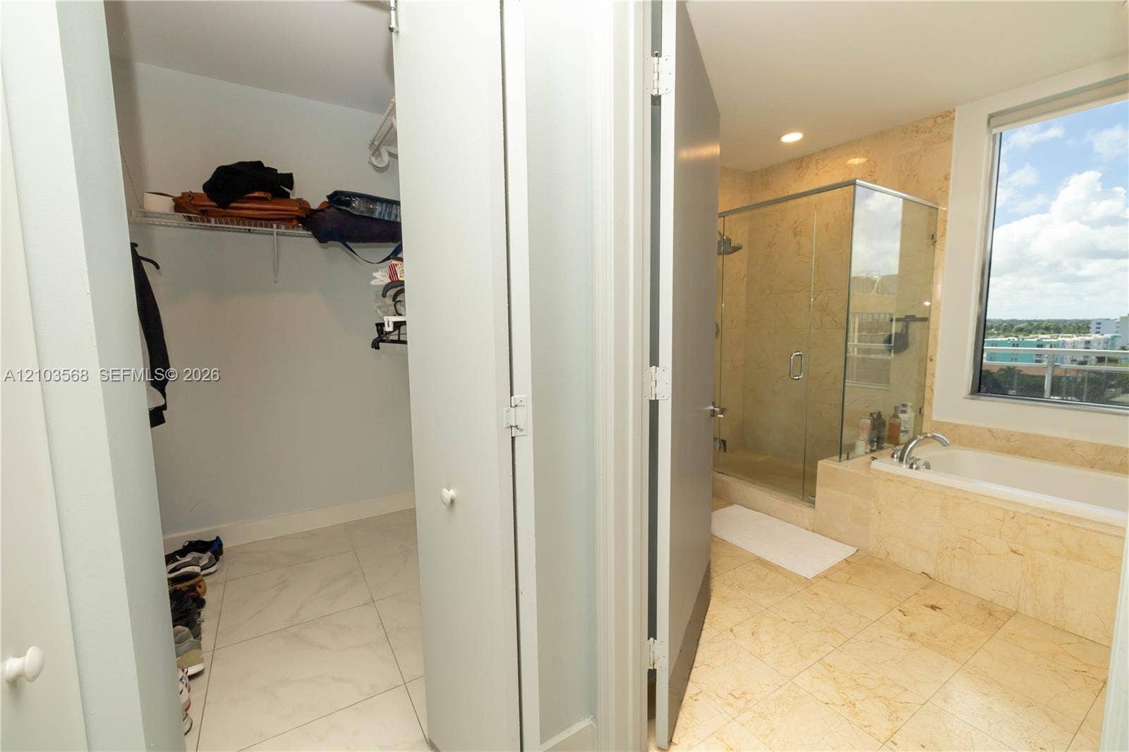 7901 Hispanola Avenue, #801, North Bay Village, FL 33141 Bathroom featuring a glass-enclosed shower, stone-surround soaking tub, stone tile flooring, and a walk-in closet with built-in shelving