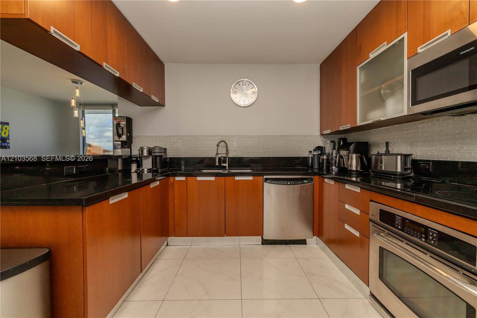 7901 Hispanola Avenue, #801, North Bay Village, FL 33141 U-shaped kitchen featuring wood-finish cabinetry, black stone countertops, stainless steel appliances, tiled backsplash, and light-toned tile flooring