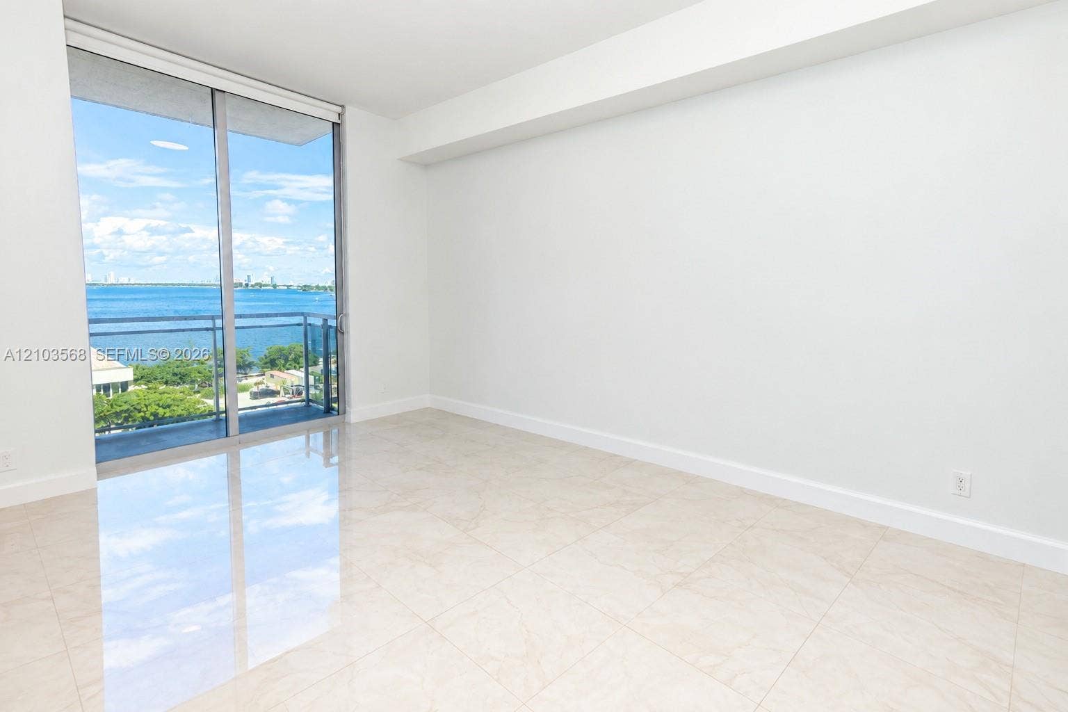 7901 Hispanola Avenue, #801, North Bay Village, FL 33141 Floor-to-ceiling sliding glass doors, balcony access, neutral stone-finish tile flooring, and water-facing scenery