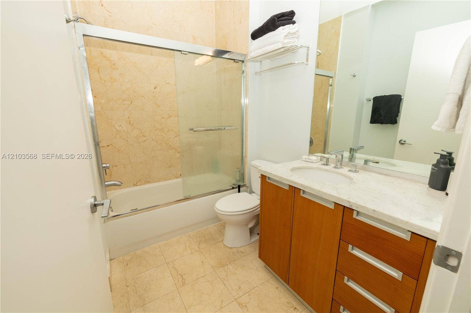 7901 Hispanola Avenue, #801, North Bay Village, FL 33141 Full bathroom featuring stone-surround tub with glass enclosure, wood-finish vanity with stone countertop, undermount sink, and wall-to-wall mirror
