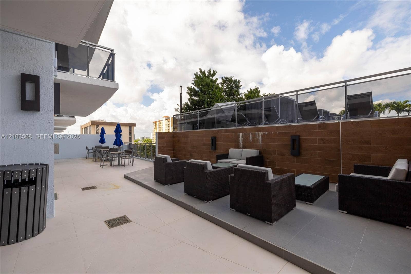 7901 Hispanola Avenue, #801, North Bay Village, FL 33141 Expansive outdoor terrace featuring large-format tile flooring, wood-finish wall cladding, glass-panel railings, and integrated wall-mounted lighting