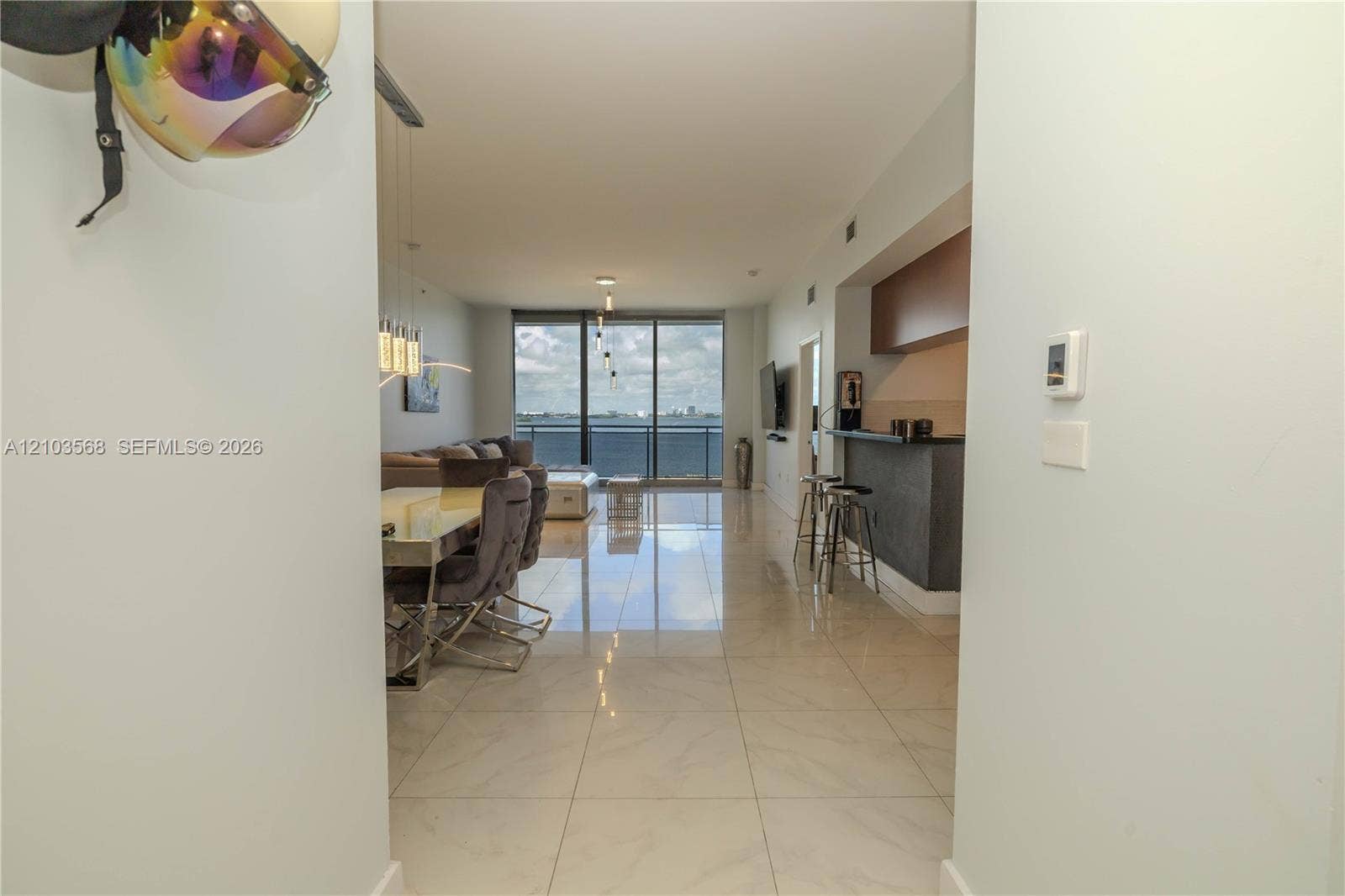 7901 Hispanola Avenue, #801, North Bay Village, FL 33141 Open-concept interior featuring large-format tile flooring, kitchen breakfast bar with integrated cabinetry, and floor-to-ceiling glass wall