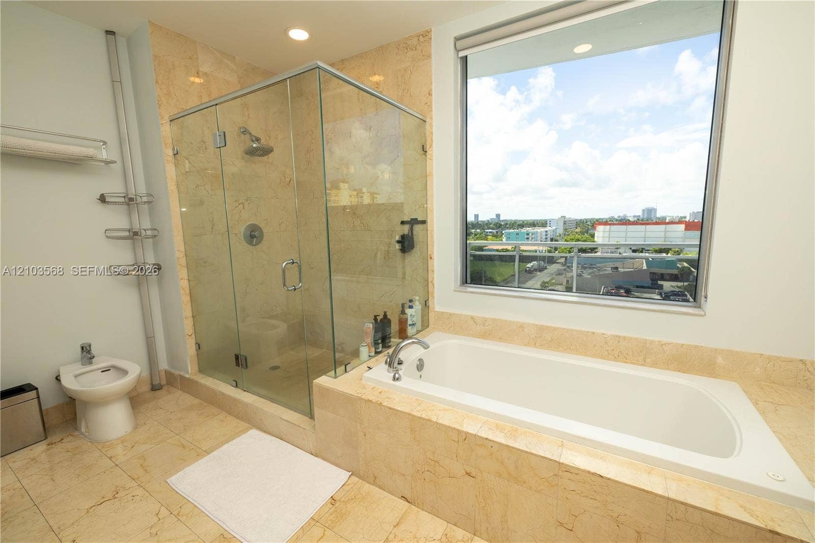 7901 Hispanola Avenue, #801, North Bay Village, FL 33141 Bathroom featuring stone-finish flooring and wall tiling, a glass-enclosed shower, a drop-in soaking tub, and a bidet