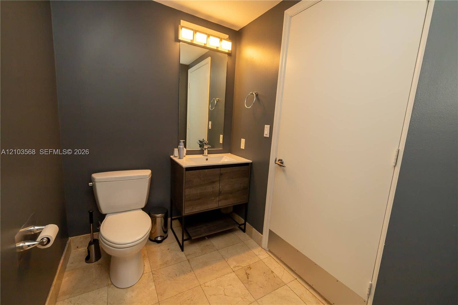 7901 Hispanola Avenue, #801, North Bay Village, FL 33141 Bathroom featuring a wood-finish vanity with a rectangular sink, integrated light fixture above a rectangular mirror, and stone-finish flooring