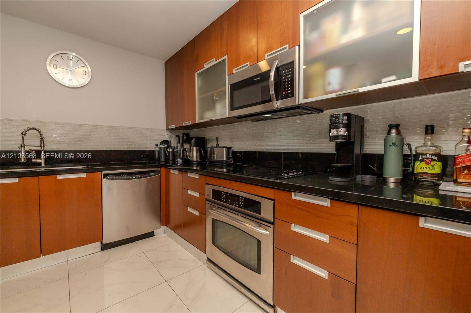 7901 Hispanola Avenue, #801, North Bay Village, FL 33141 Kitchen featuring flat-panel wood cabinetry, black countertops, stainless steel appliances, tiled backsplash, and light-toned flooring