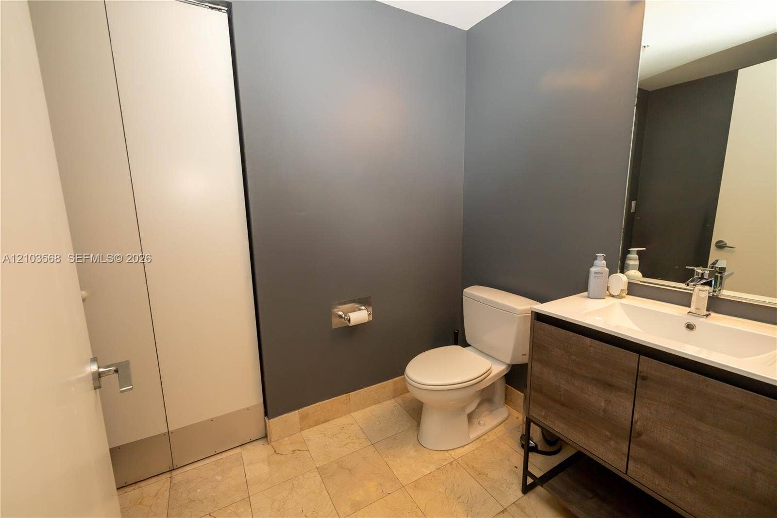 7901 Hispanola Avenue, #801, North Bay Village, FL 33141 Modern vanity featuring a wood-finish cabinet with a white countertop and rectangular basin, paired with natural stone floor tiling and large-format wall mirror