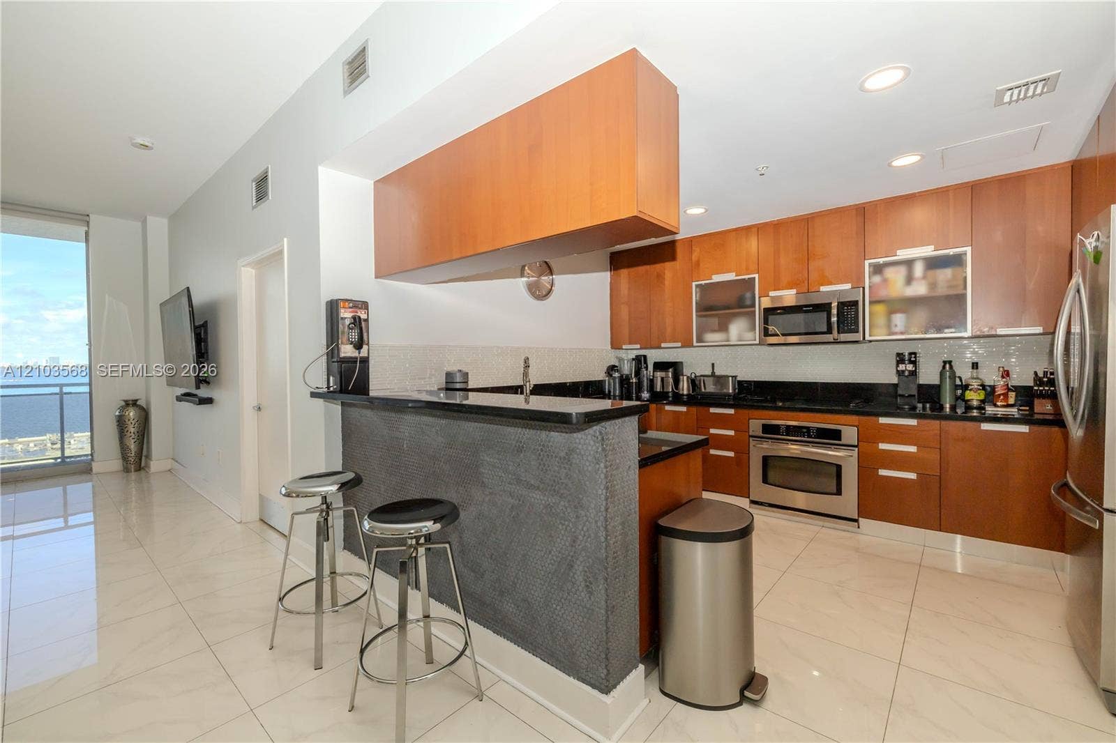 7901 Hispanola Avenue, #801, North Bay Village, FL 33141 Kitchen featuring wood cabinetry, stone countertops, stainless steel appliances, and a tiled breakfast bar