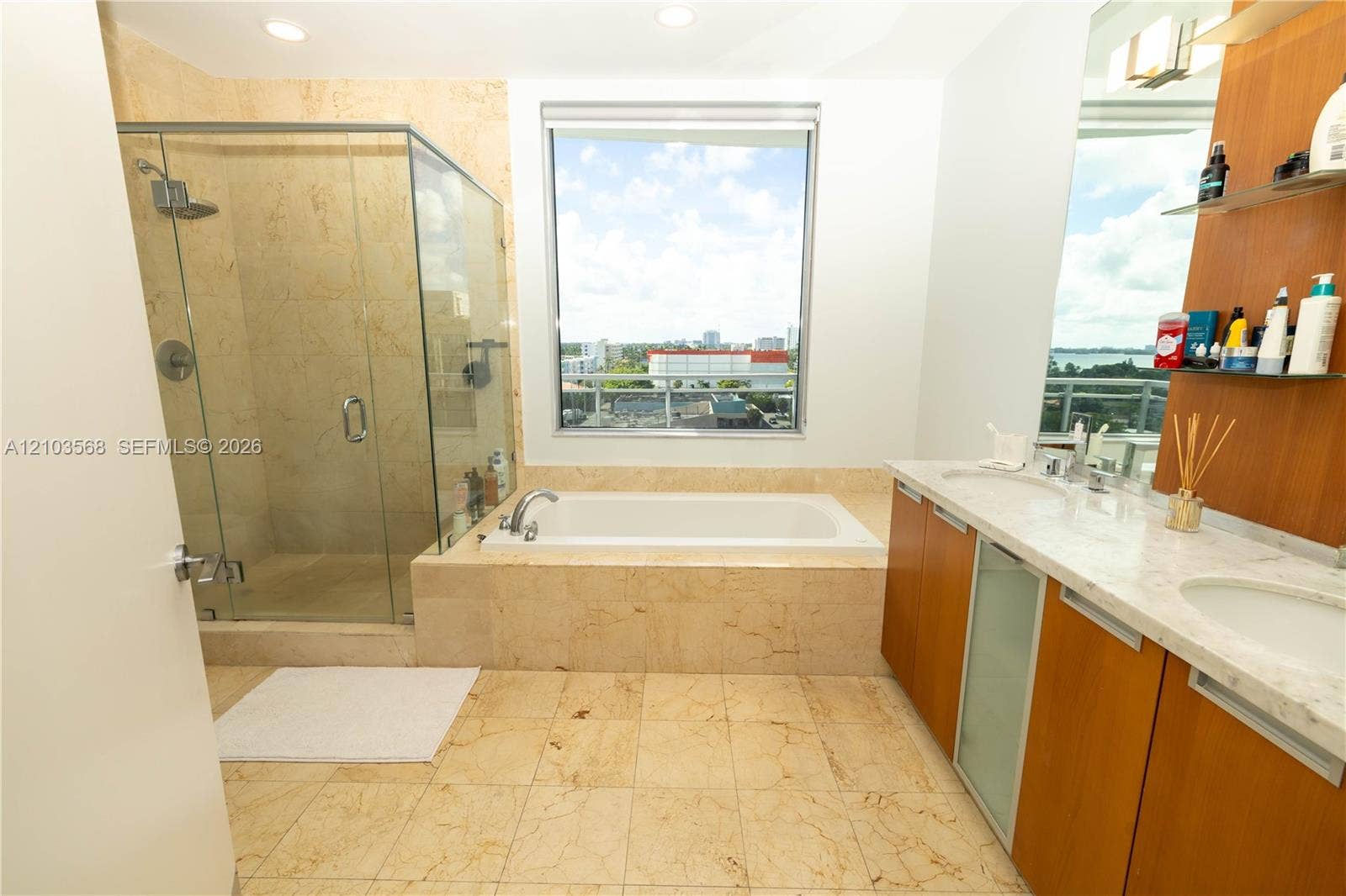 7901 Hispanola Avenue, #801, North Bay Village, FL 33141 Bathroom featuring a glass-enclosed shower, built-in soaking tub, dual-sink vanity with stone countertop, and wood-finish cabinetry