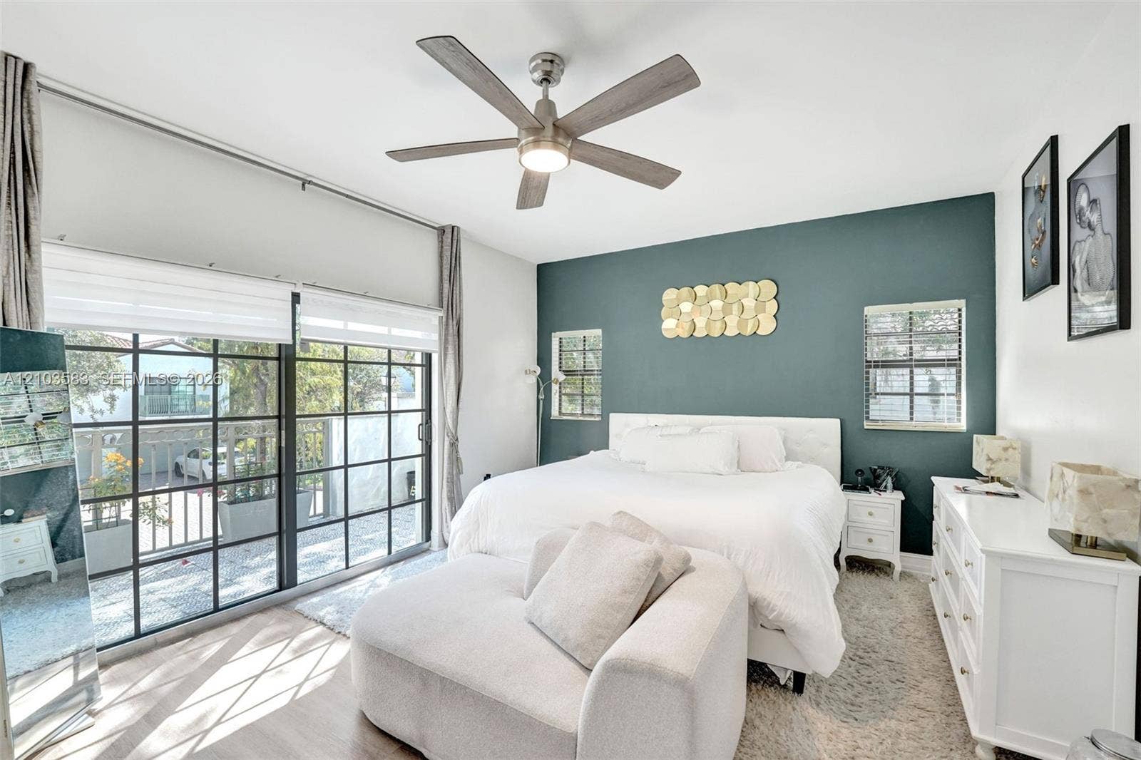 Bedroom featuring floor-to-ceiling grid-style sliding glass doors, wood-finish flooring, a contemporary multi-blade ceiling fan with integrated lighting, and a distinct teal accent wall