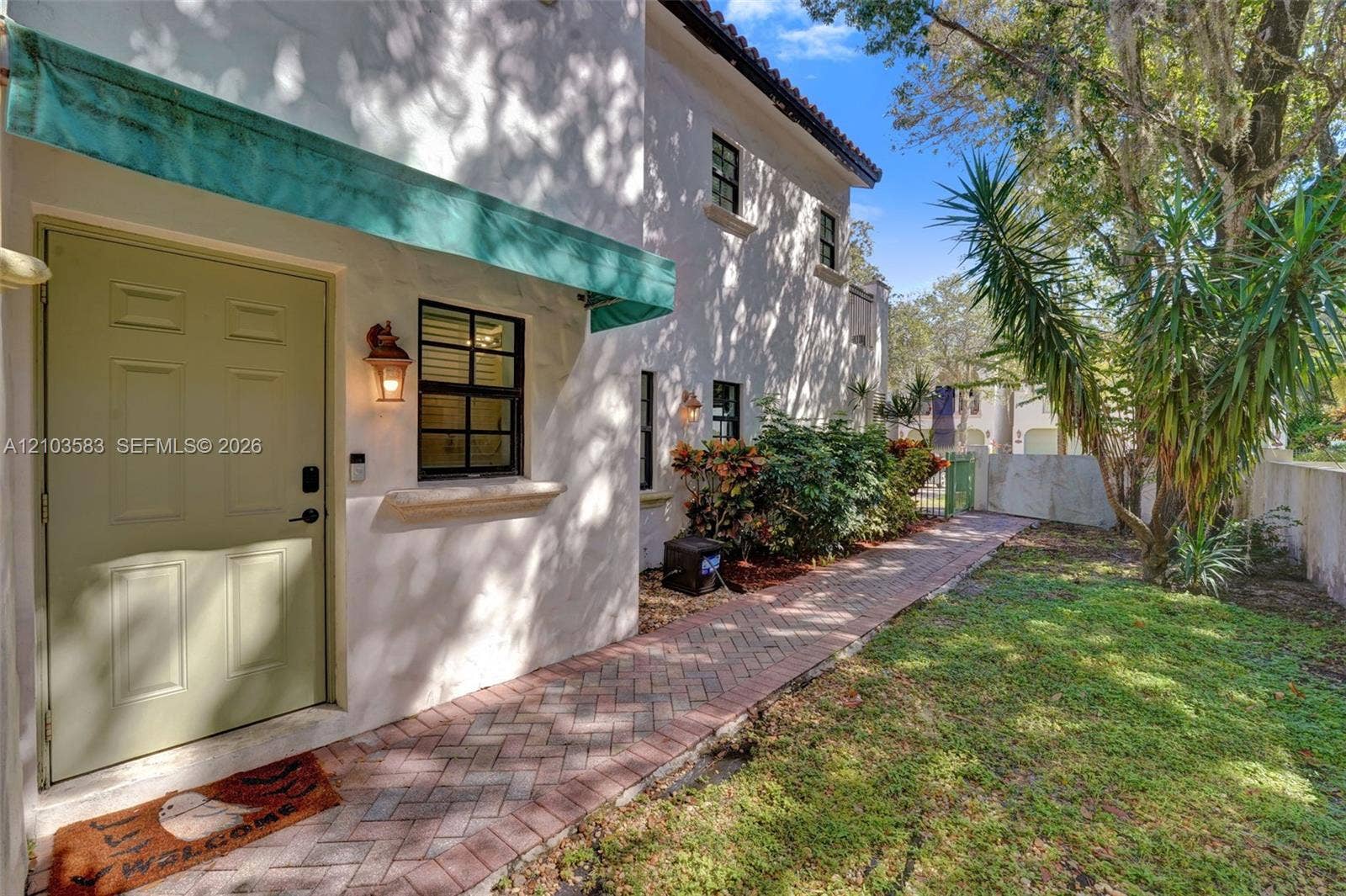 Stucco exterior featuring a herringbone-patterned brick walkway, green fabric awning, and decorative wall-mounted lighting