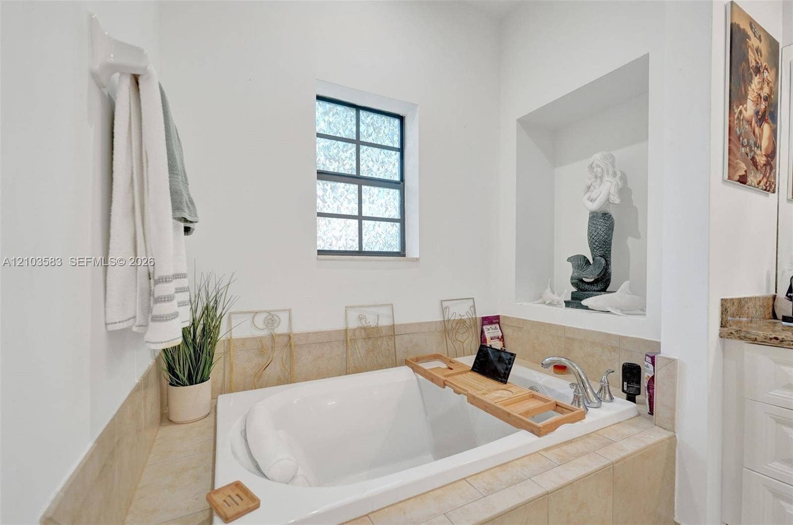 Drop-in soaking tub with a tiled surround, chrome faucet, and recessed wall niche