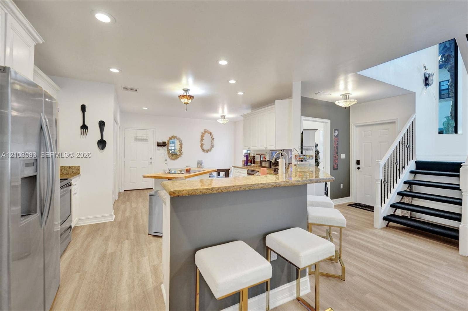 Kitchen featuring stone-surfaced breakfast bar, white cabinetry, stainless steel refrigerator, recessed lighting, and wood-finish flooring
