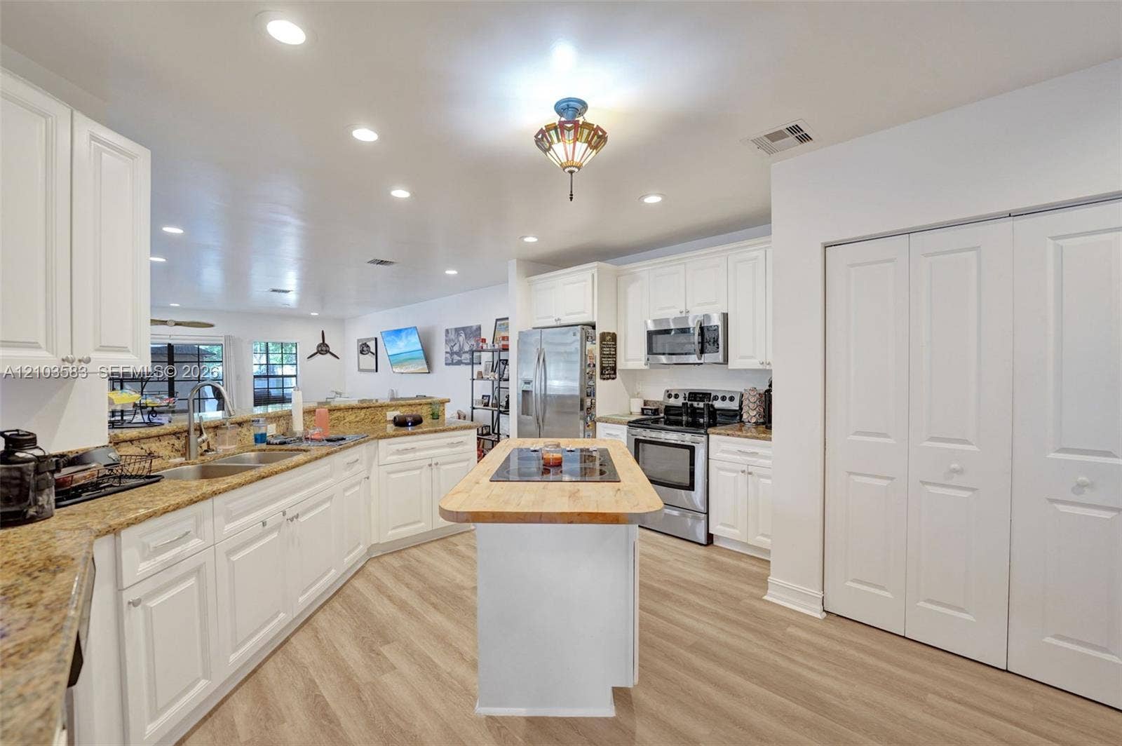Kitchen featuring white cabinetry, stone countertops, a center island with a cooktop, stainless steel appliances, and wood-finish flooring